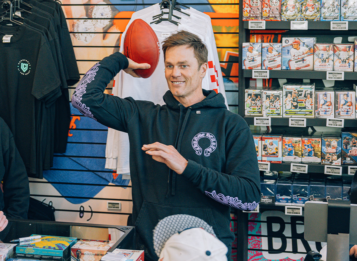 Man holding a football inside CardVault Brooklyn, surrounded by sports cards and apparel