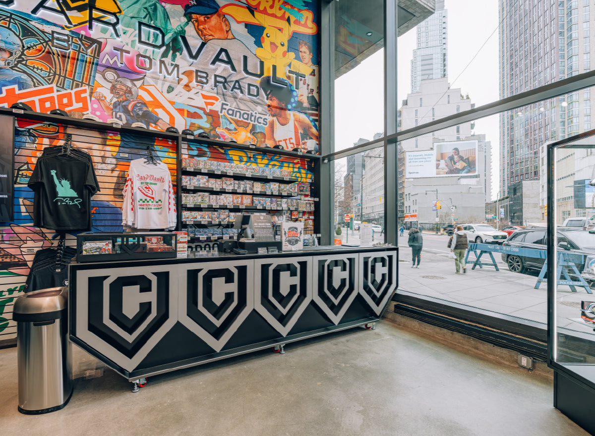 CardVault Brooklyn interior with sports card displays, merchandise, colorful sports mural, and city street visible through windows