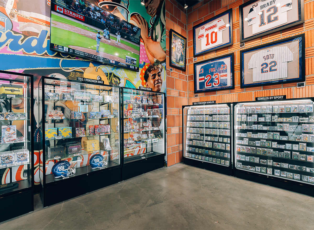 CardVault Brooklyn interior featuring sports card displays, memorabilia jerseys, and a baseball game on TV